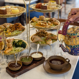 Tiered afternoon tea stand with Indian-inspired canapés, samosas and sweets, served with tea in an ornate teapot
